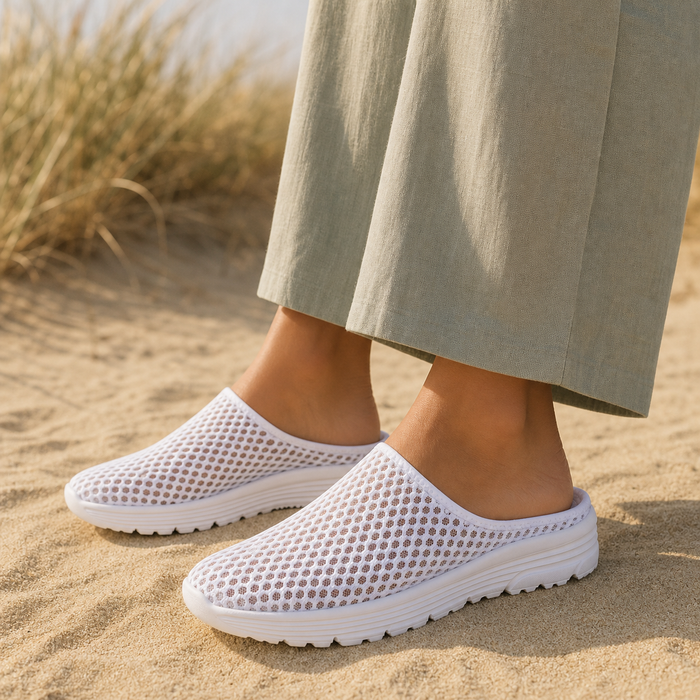 White Airomi mesh mules worn on dry beach sand among dune grass
