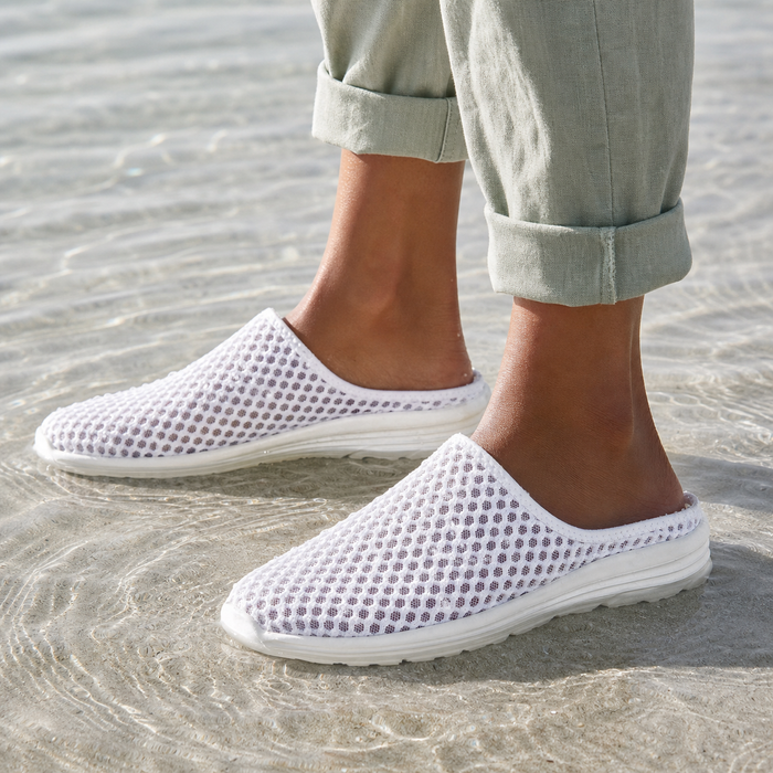 White Airomi mesh mules worn ankle-deep in clear shallow water